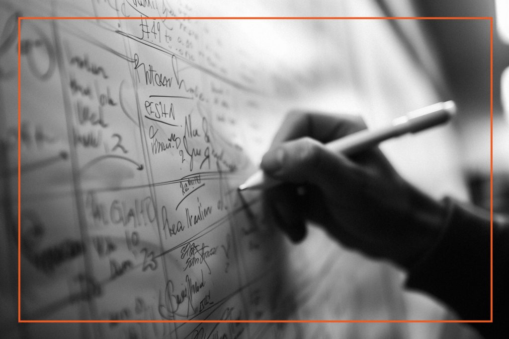 A hand writing on a whiteboard filled with notes and signatures, representing planning and organization in the context of cultural change, leadership, and execution.