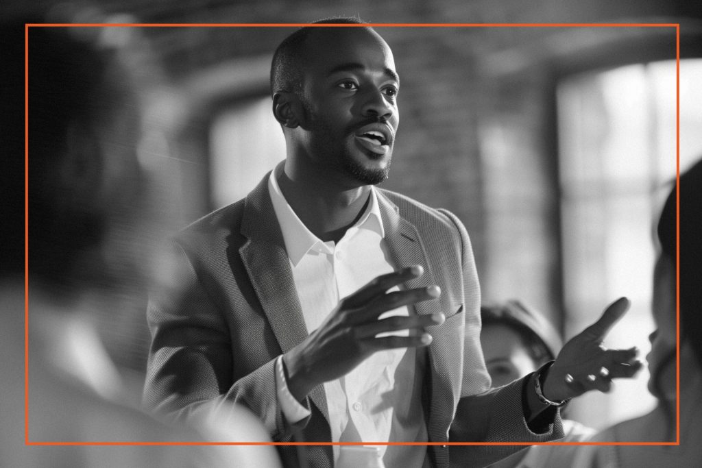 A professional man in a business suit is passionately speaking to an audience, illustrating leadership and cultural change in a modern workplace setting.